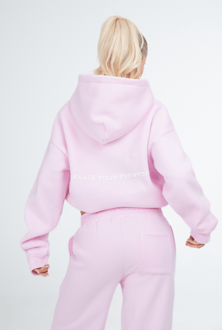 Person wearing a pink hoodie and pants set on a white background
